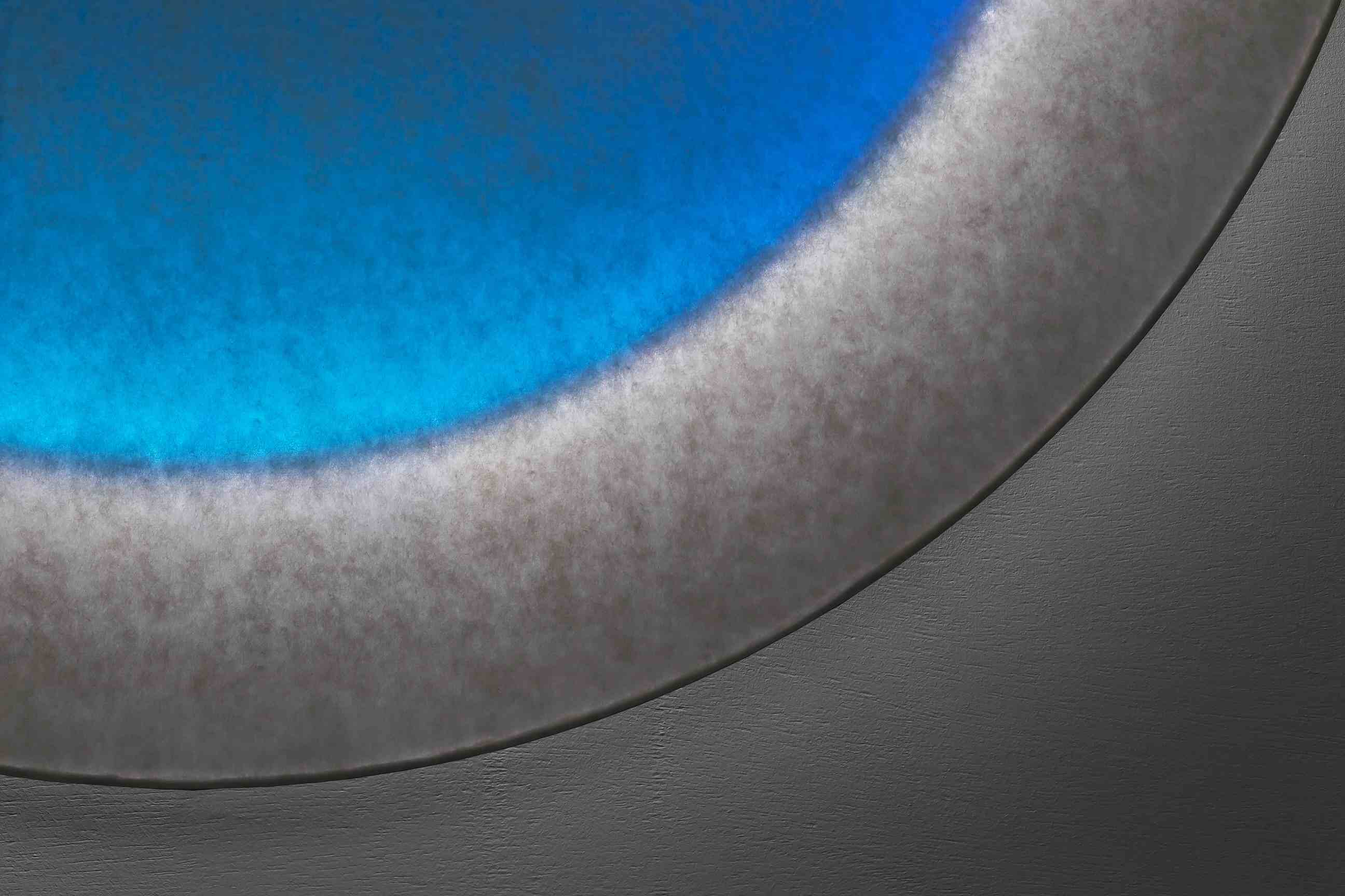 Nahaufnahme der Moodmoon Wandleuchte: Rundes Design mit blauem Lichteffekt und grauer Oberfläche.