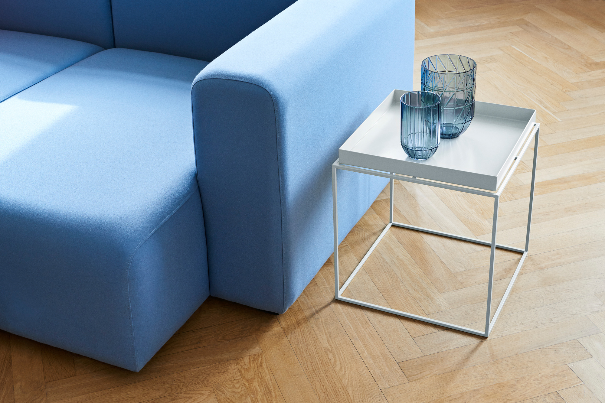 Heller Hay Tray Table Beistelltisch mit zwei blauen Glasvasen neben einem blauen Sofa.