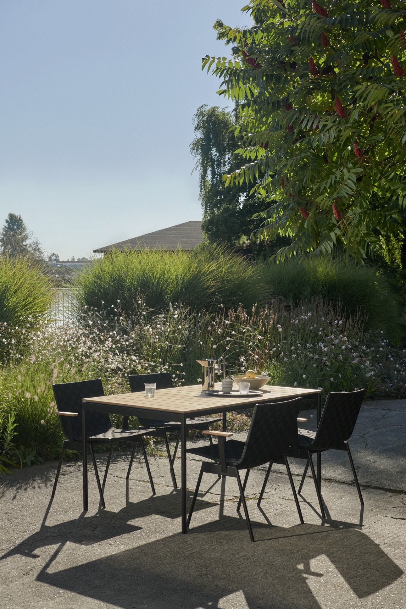 AndTradition Ville AV25 Outdoor Tisch mit vier Stühlen im Garten, gedeckt mit Getränken und Obst.