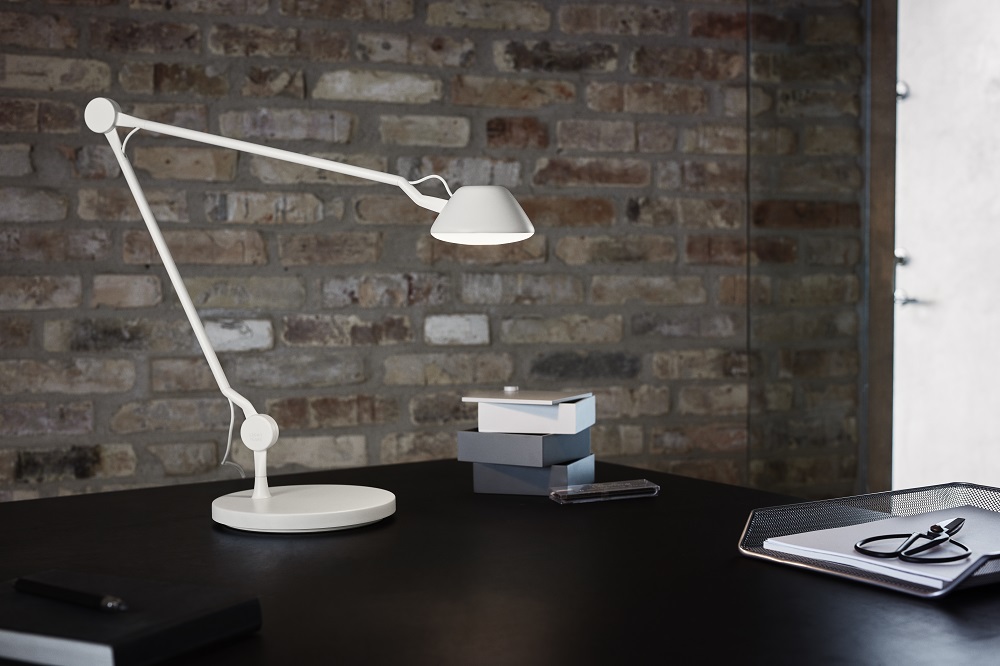 Weiße AQ01 Tischleuchte von Fritz Hansen auf schwarzem Schreibtisch vor Backsteinwand. Design Lampe.