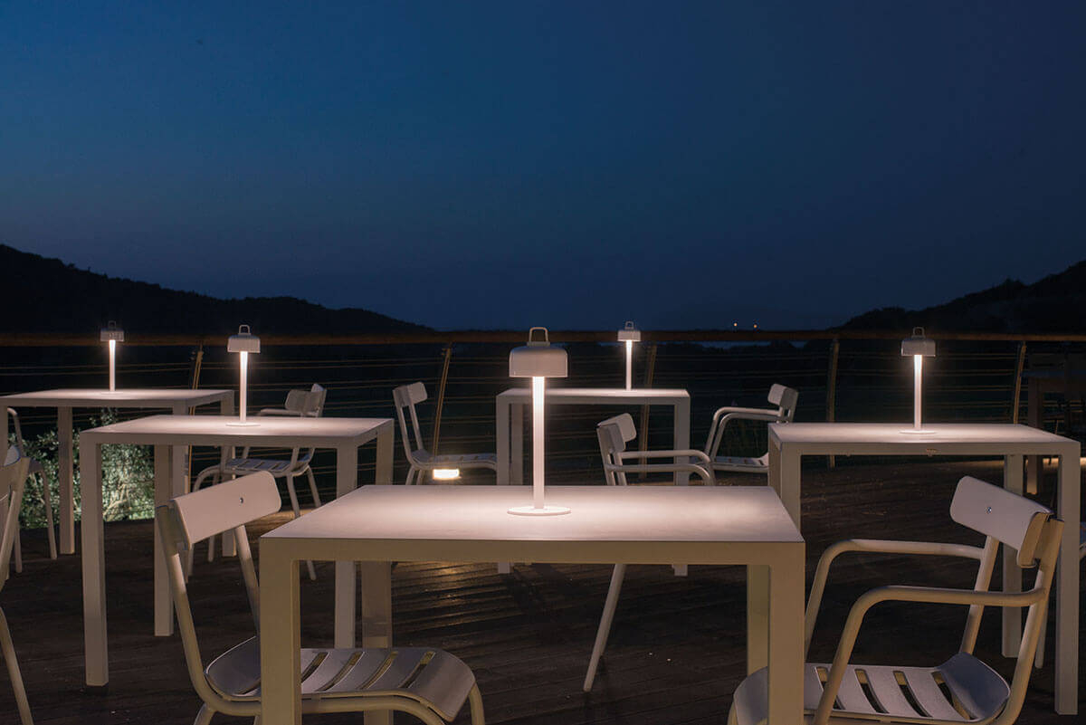 Mehrere kleine Luciole Outdoor Leuchten von Emu auf Tischen im Freien bei Nacht.