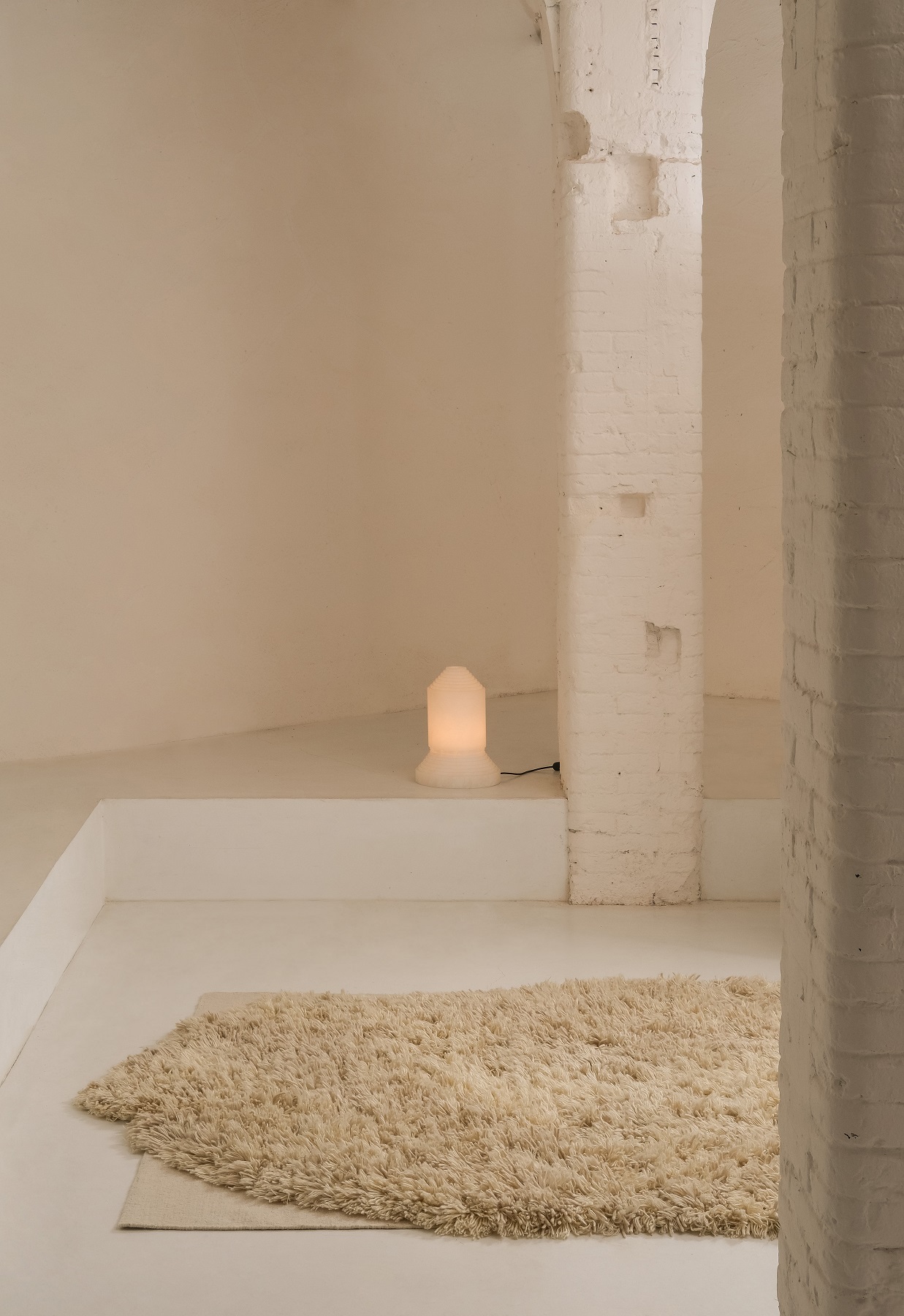 Beiger Alga Rug Teppich von Nanimarquina in minimalistischem Raum mit Lampe und weißen Wänden.