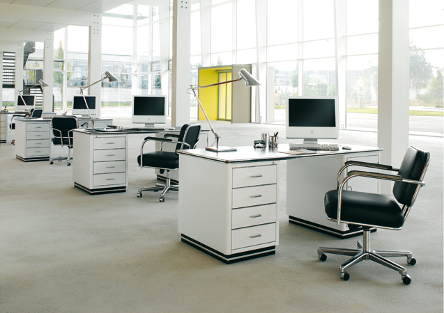 TB 228 Classic Line Schreibtische von Müller Möbelfabrikation in einem hellen Büro mit großen Fenstern.