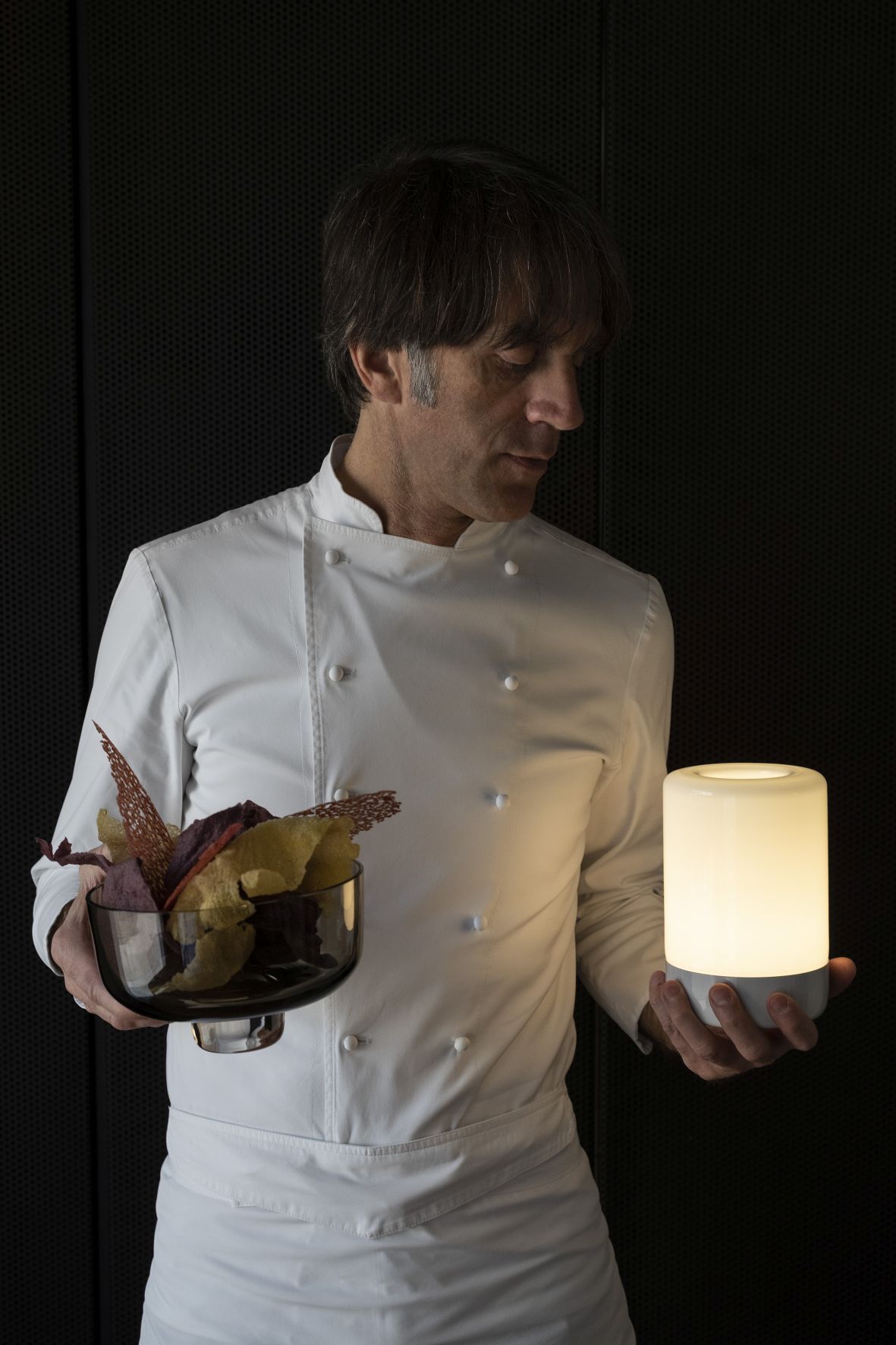 Koch hält Bontà Akkuleuchte von Artemide und Schale mit Chips. Tischleuchte in Topas.