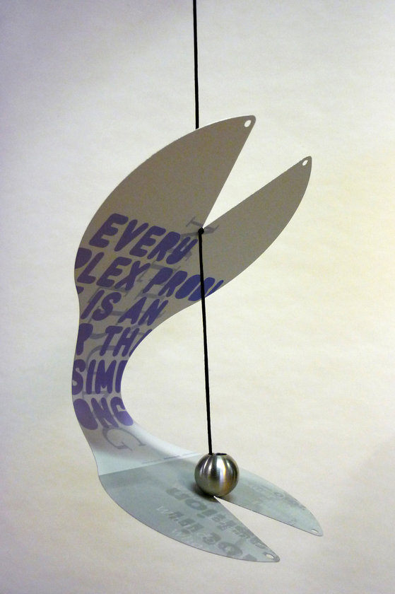 Nahaufnahme der Vogelstation von Daniel Grimme, ein hängendes Mobile mit Text und Metallkugel, modernes Design.