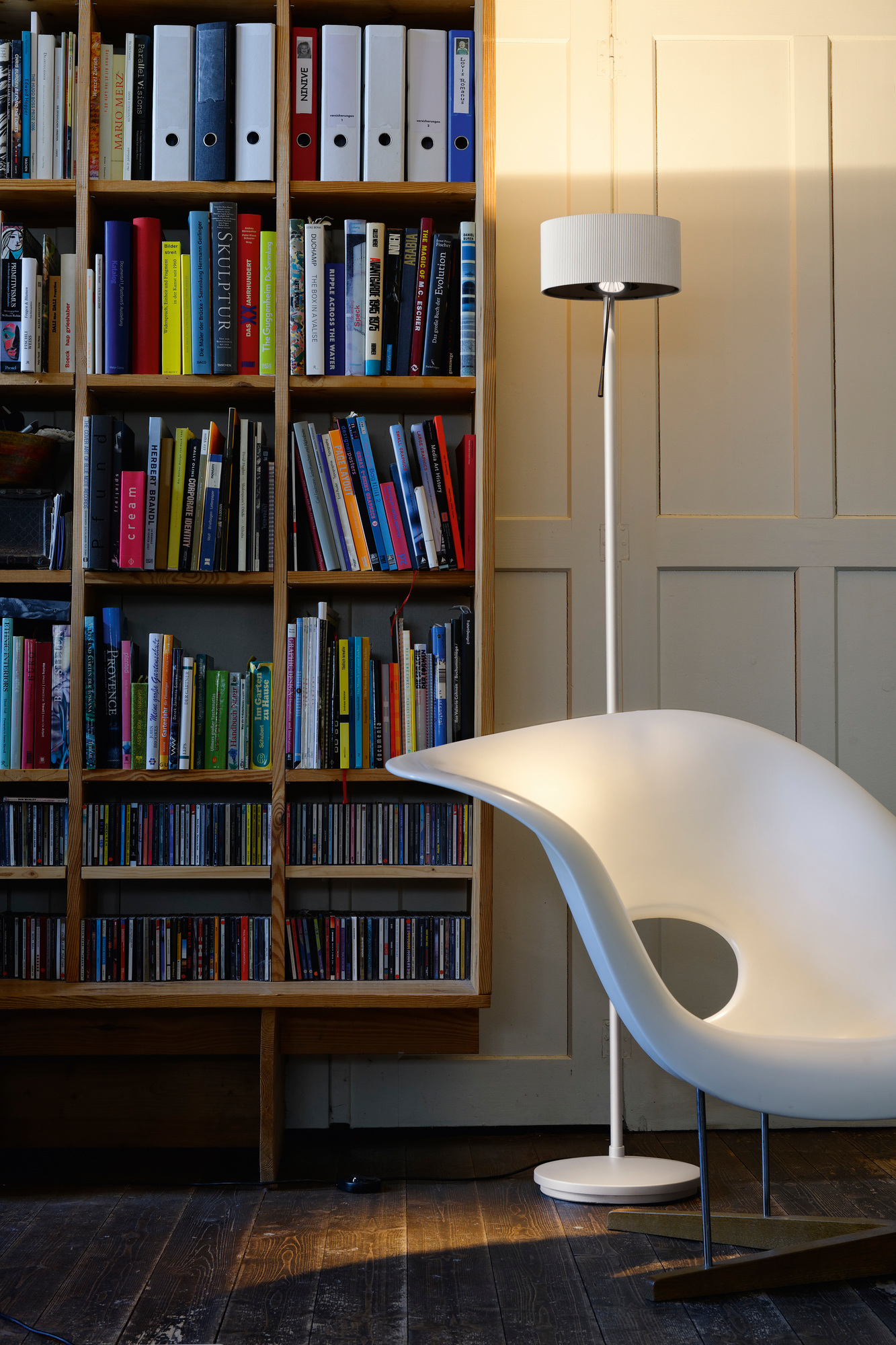 Diogenes LED Stehleuchte von Belux in Goldgrau neben Bücherregal und Design-Sessel. Moderne Beleuchtung.