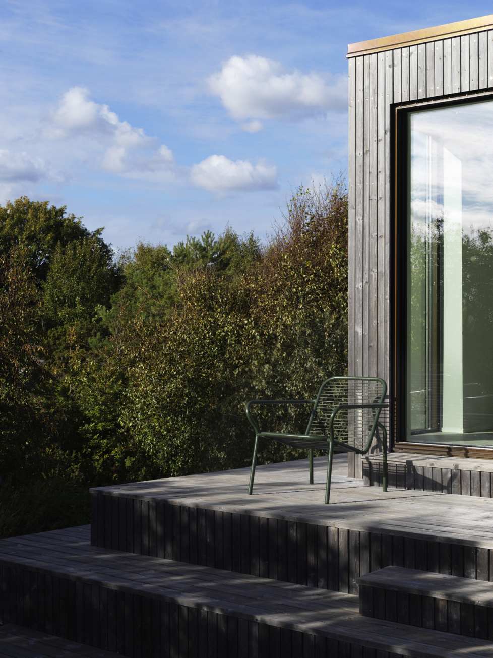 Grüner Vig Lounge Chair Sessel von Normann Copenhagen auf Holzterrasse vor modernem Haus.