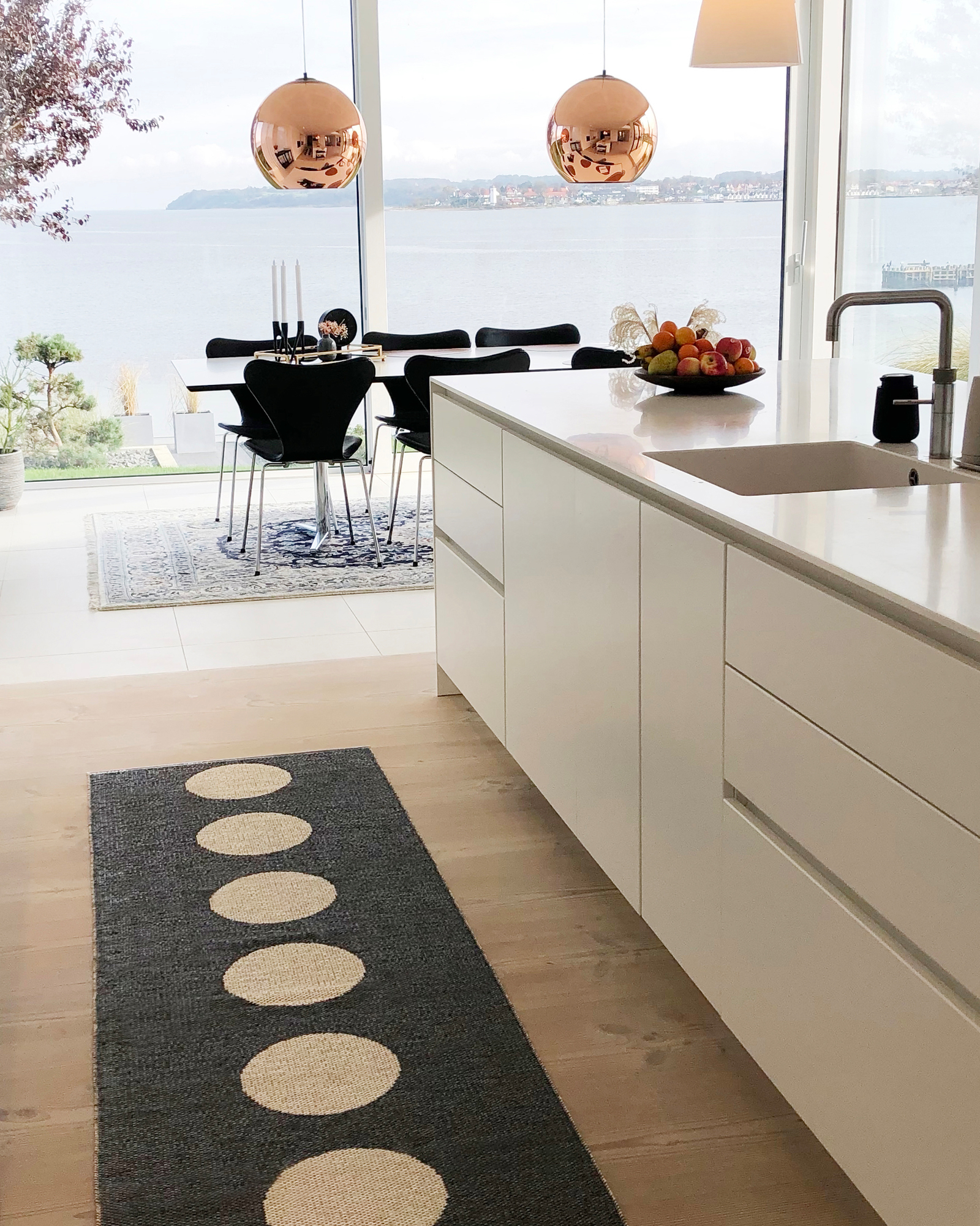 Vera Kunststoffteppich von Pappelina, dunkelgrauer Teppich mit weißen Kreisen in moderner Küche mit Meerblick.