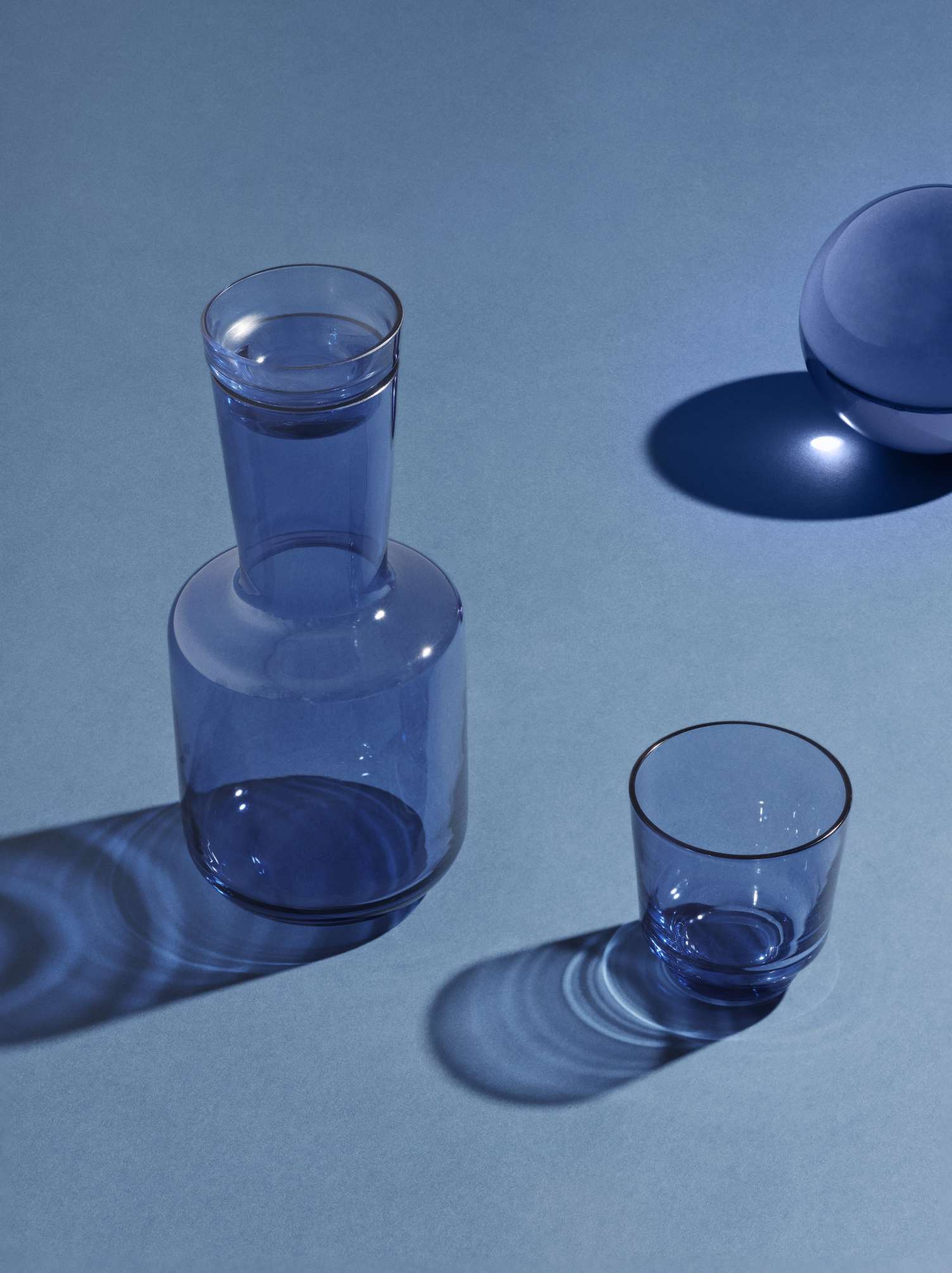 Blaue Raise Karaffe von Muuto mit passendem Glas auf blauem Hintergrund.