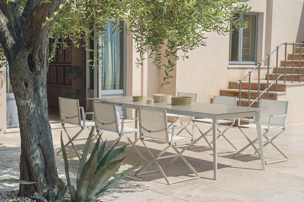 Weißer Ciak Regiestuhl von Emu neben einem Gartentisch im Außenbereich unter einem Olivenbaum.