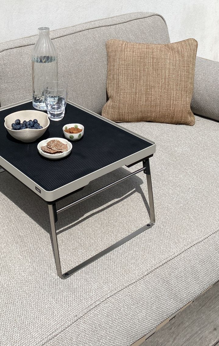 Vipp Tray Tisch für den Außenbereich auf einer Couch mit Getränken und Snacks.
