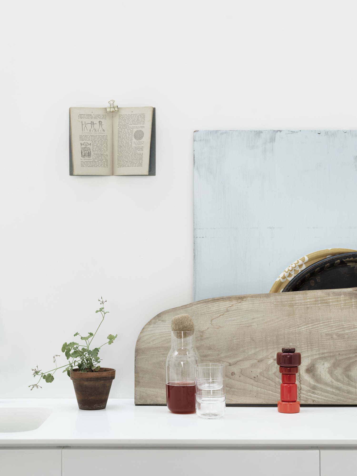 Stillleben mit Corky Karaffe, Glas, Pflanze und Buch auf weißer Oberfläche. Muuto Design.