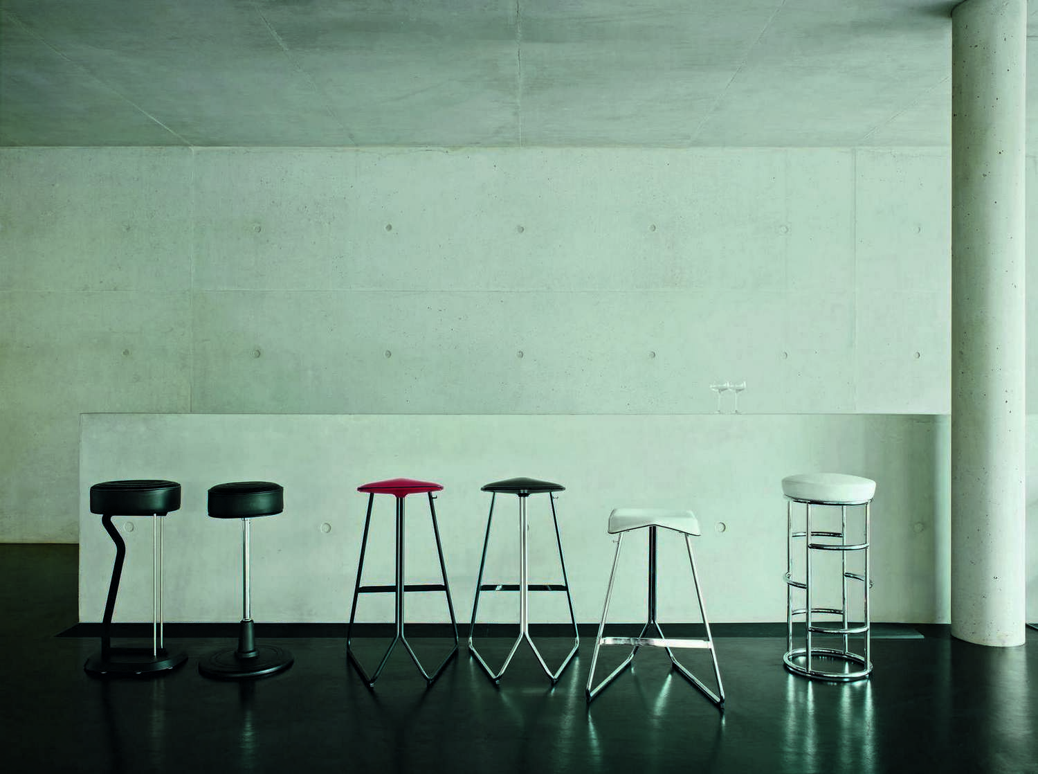 Verschiedene Satish Barhocker von ClassiCon in Schwarz, Rot und Weiß vor einer Betonwand.