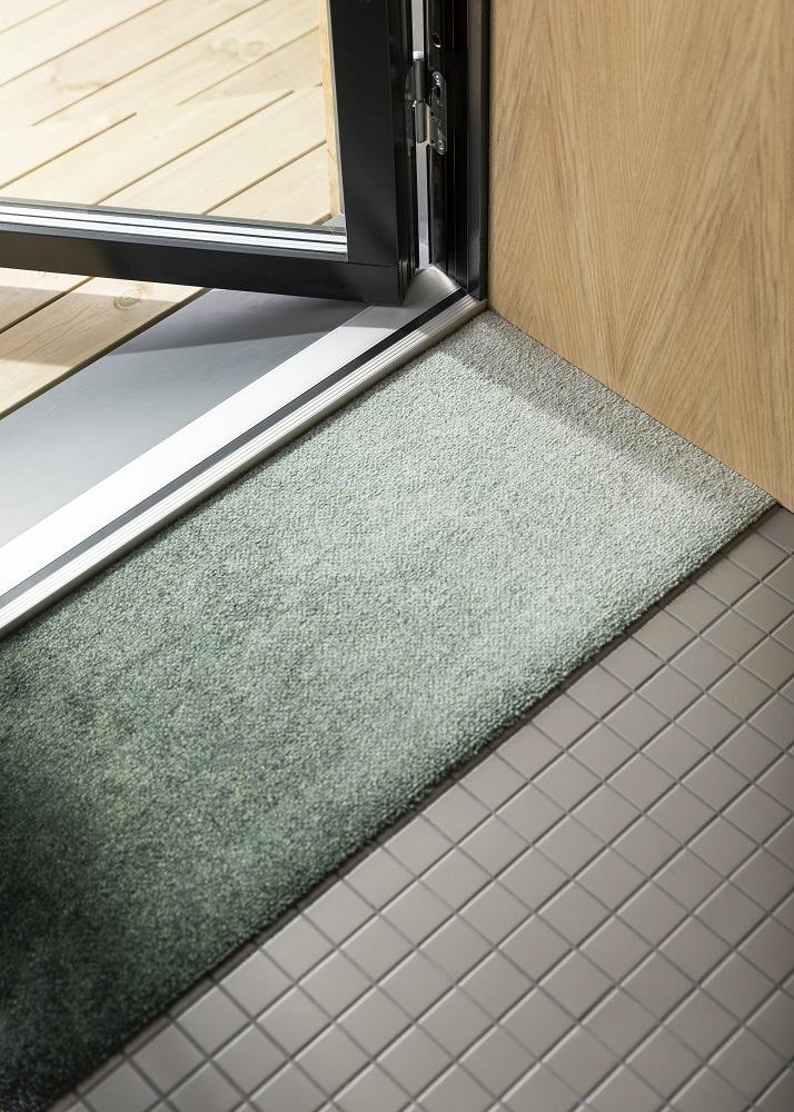 Nahaufnahme der Dis Heymat Ocean Fußmatte in Grün vor einer Tür.