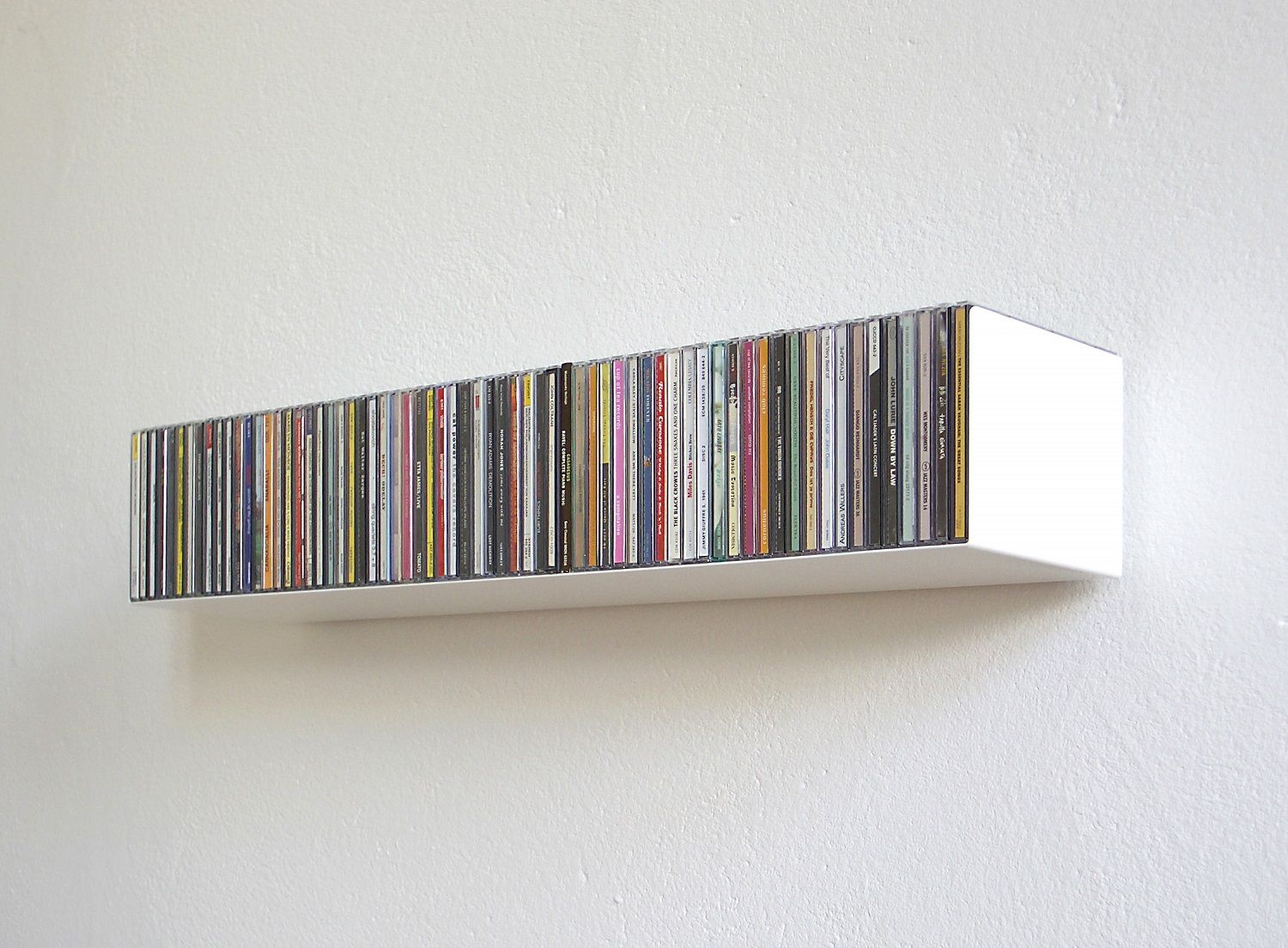 Weißes CD-Regal Linea1 von Müller Möbelwerkstätten, gefüllt mit CDs, an einer weißen Wand.