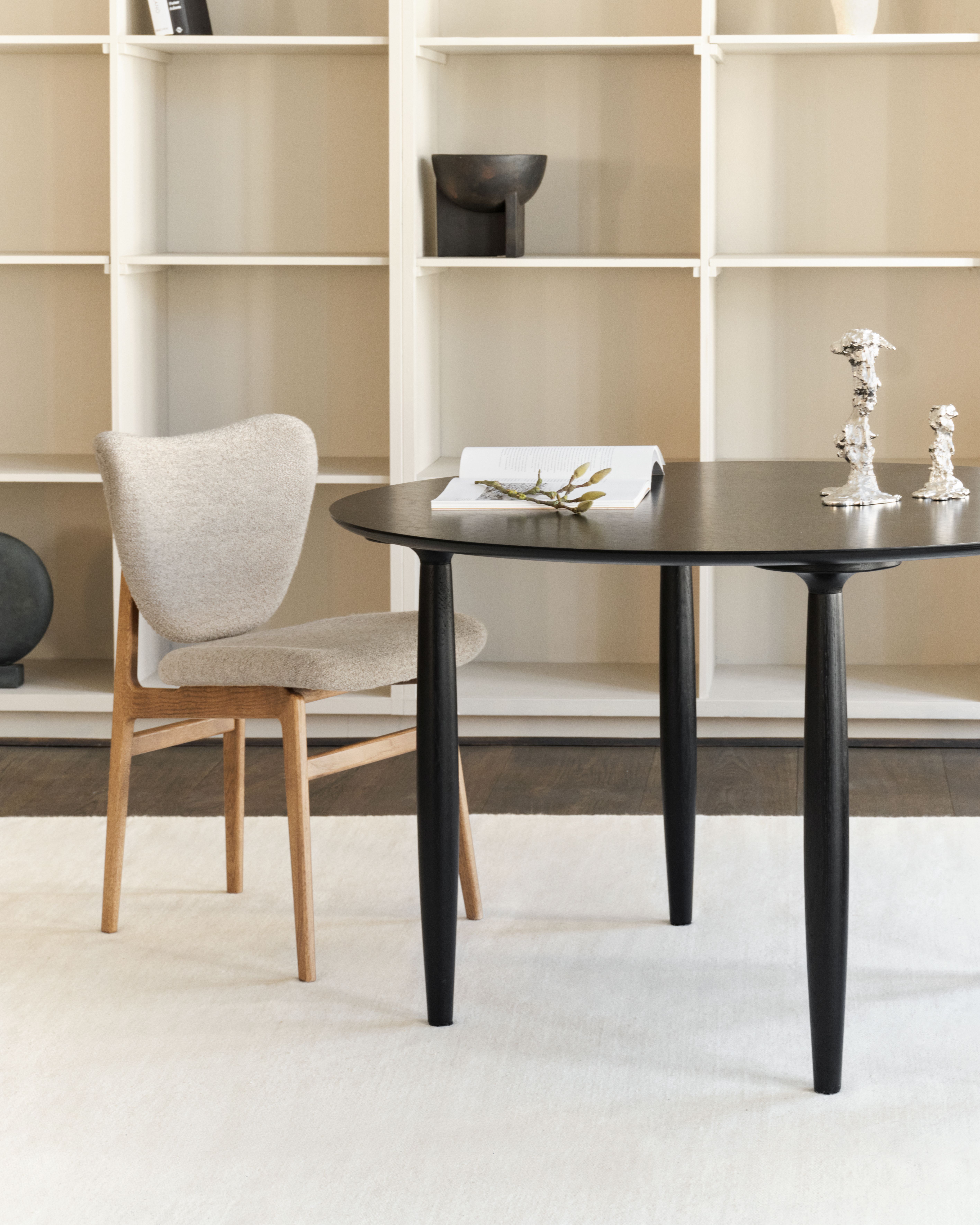 Oku Esstisch rund Eiche schwarz von Norr11 mit Stuhl und Dekoration vor Regal.