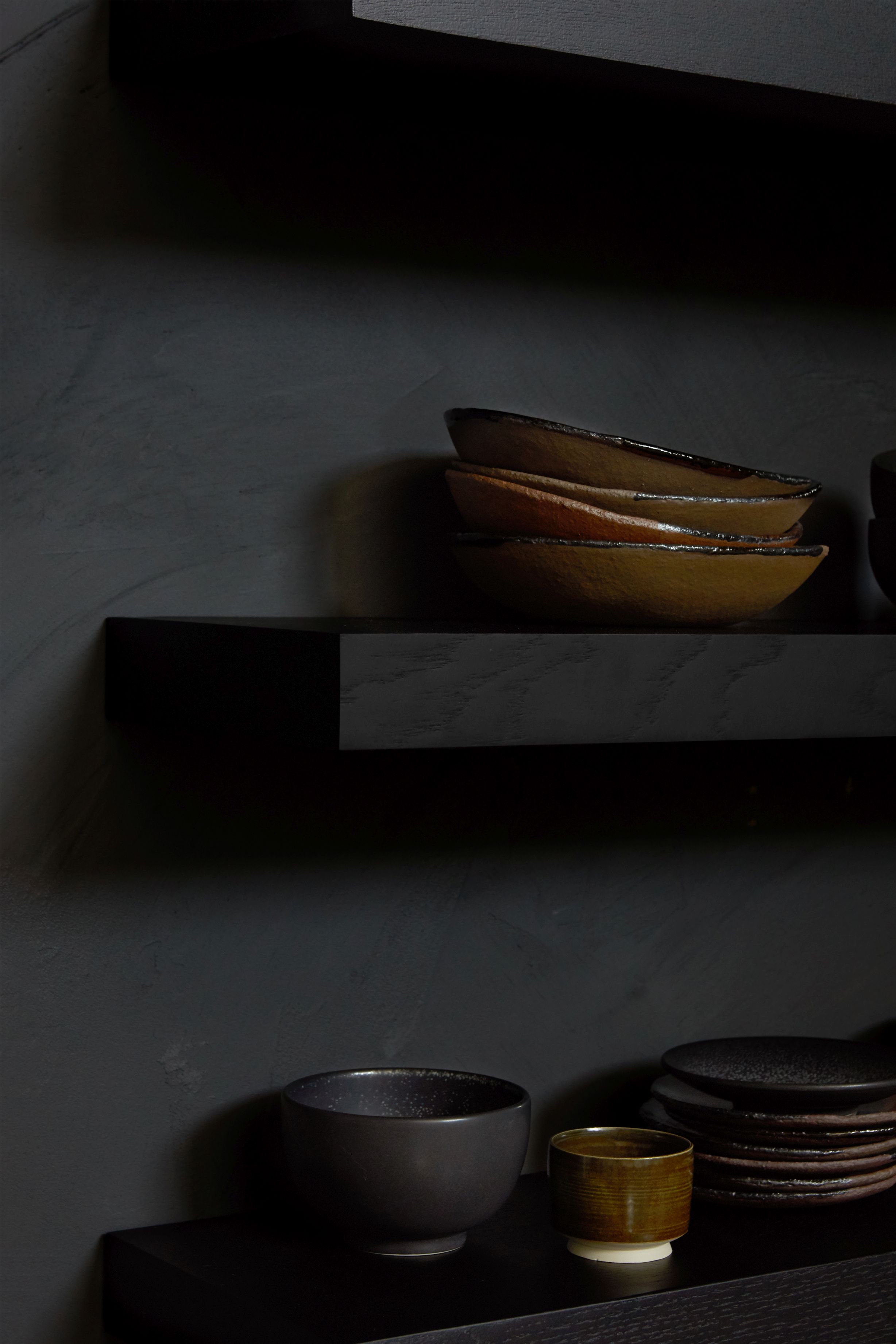 Schwarzes Ethnicraft Wandregal aus Eiche mit dekorativen Schalen und Schüsseln im modernen Ambiente.