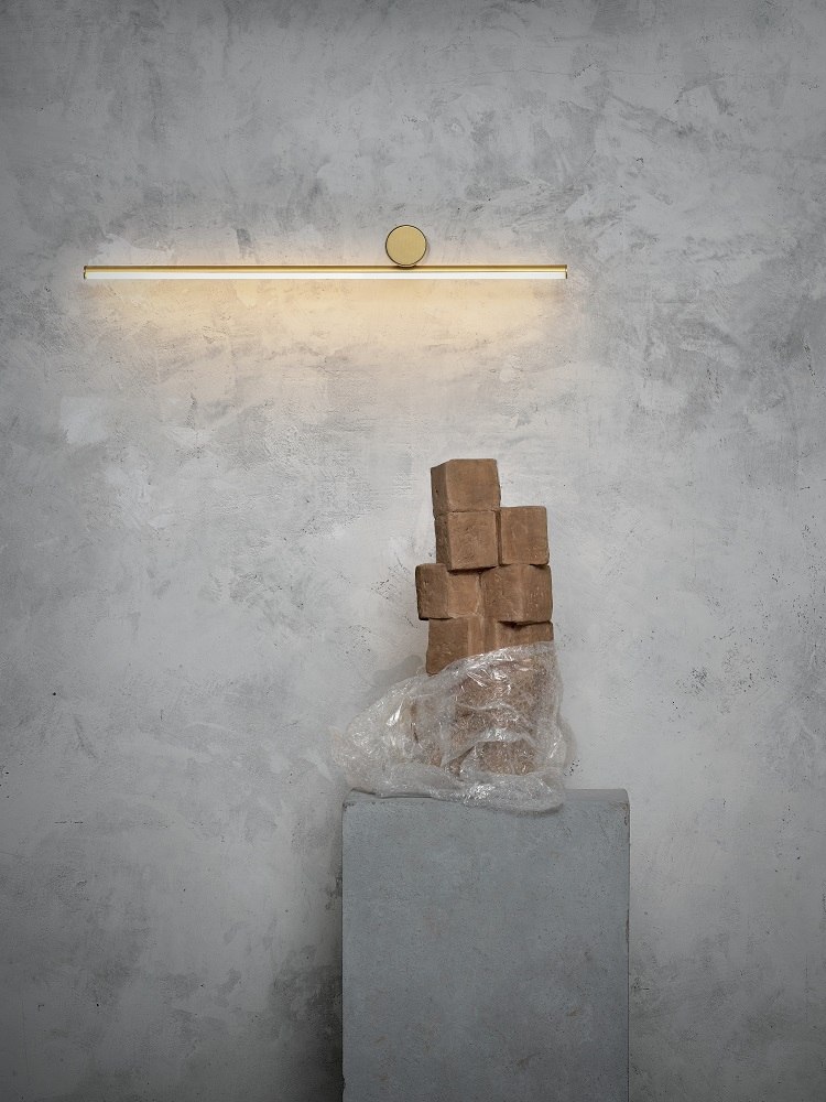 Goldene Coordinates Wall 1 Lamp Wandleuchte von Flos an grauer Wand, darunter ein Stapel brauner Würfel.