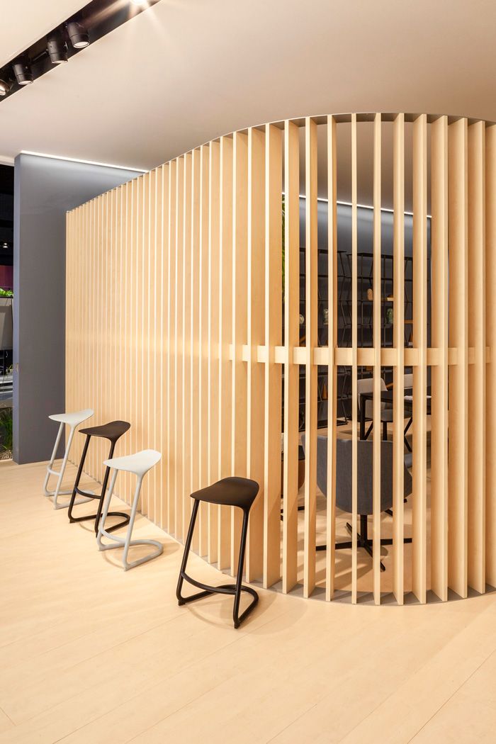 Vier moderne Barhocker in Schwarz und Weiß vor einer hölzernen Raumtrennung im Büro.