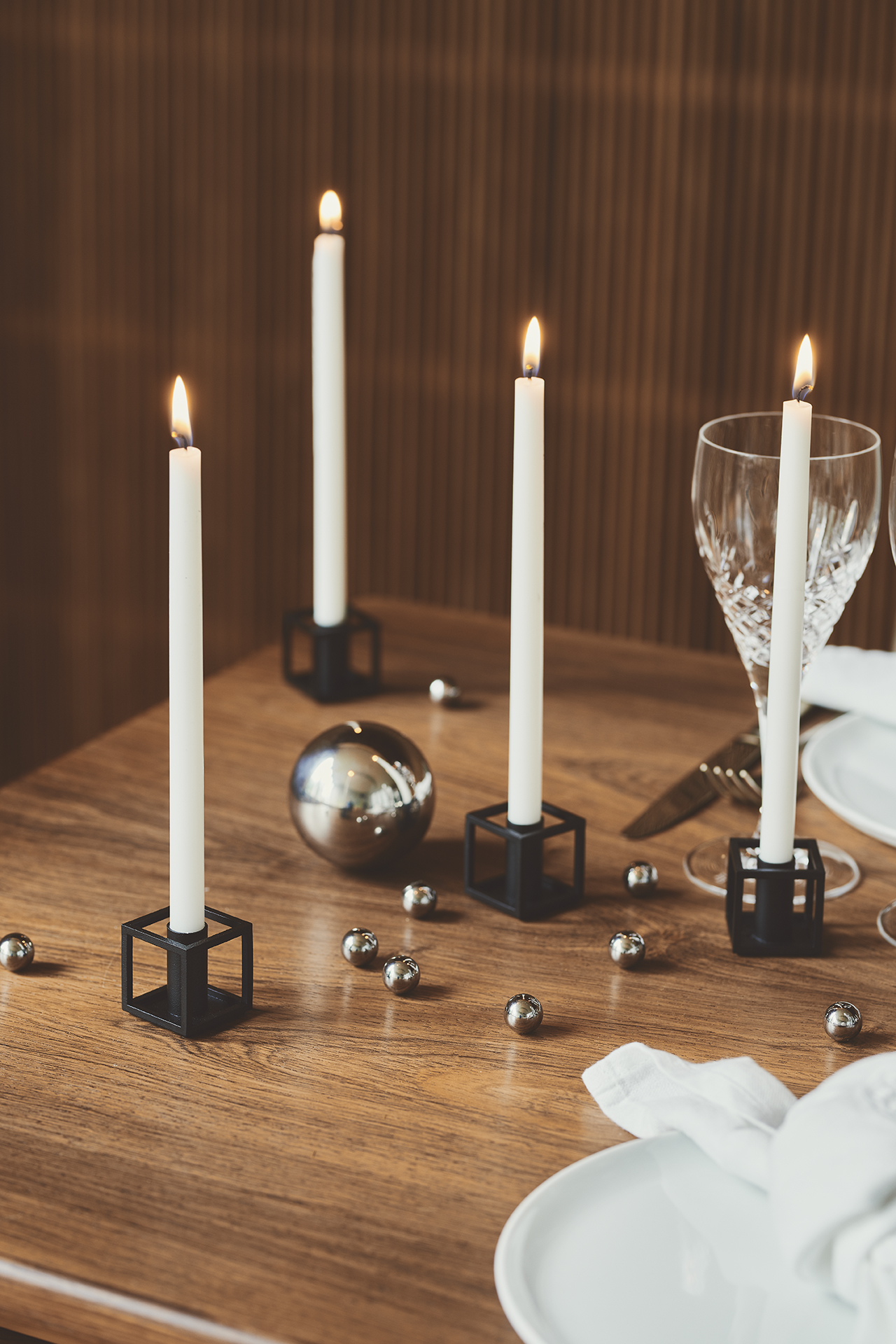 Dekorativer Tisch mit brennenden, weißen Stabkerzen in schwarzen Kerzenhaltern und silbernen Kugeln.