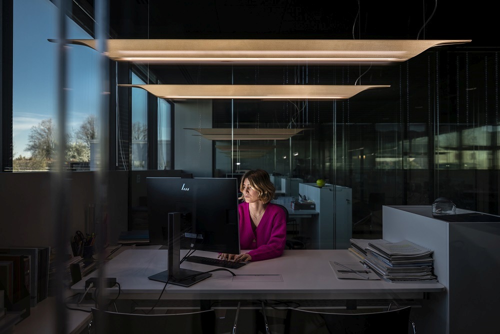 Frau arbeitet unter der Foscarini Troag Media LED Hängeleuchte im Büro, modernes Design.