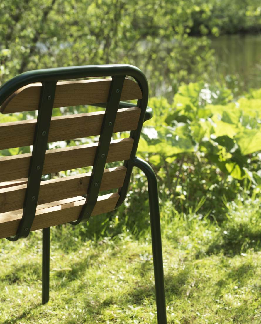 Rückansicht des Vig Armchair Wood Armlehnstuhls von Normann Copenhagen im Garten, Fokus auf Holzlehne und grüne Stahlbeine.