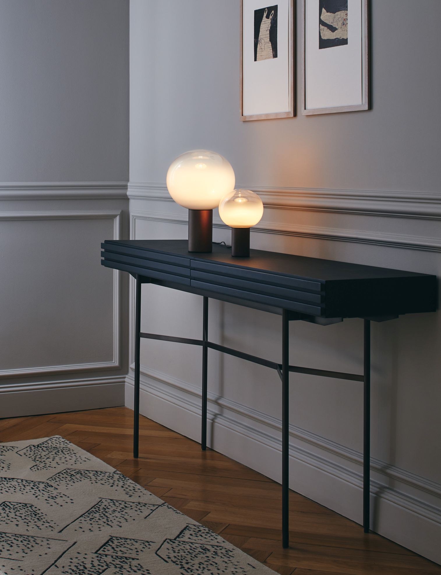 Laguna Tischleuchte von Artemide in Bronze auf schwarzem Konsolentisch mit zwei leuchtenden Kugeln.