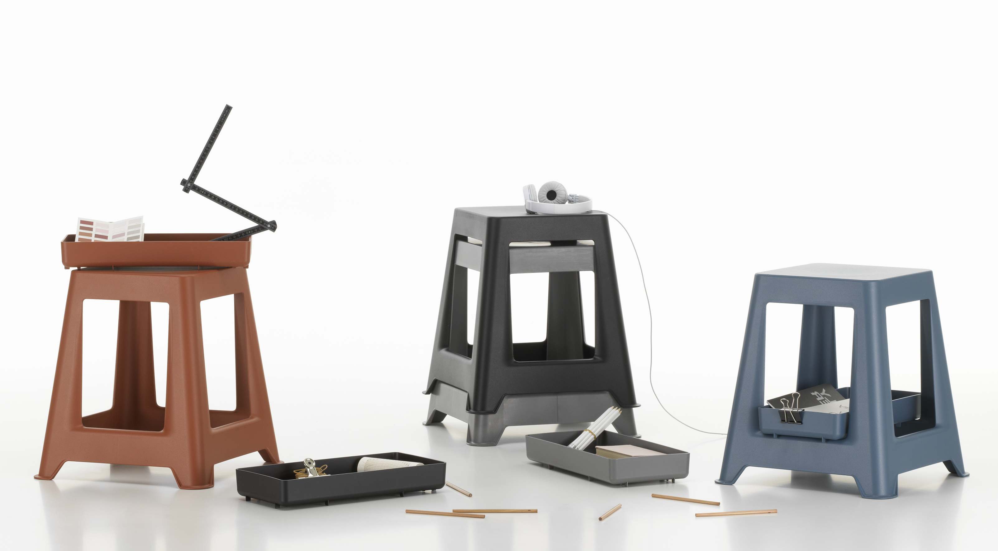Drei Chap Hocker von Vitra in Braun, Grau und Blau mit Ablagefächern für Bürobedarf.