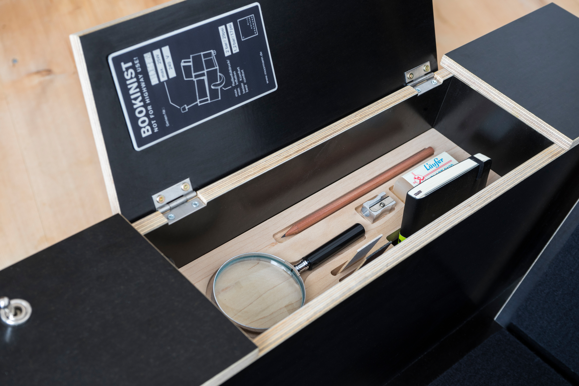 Detailaufnahme: Bookinist Lesesessel von Nils Holger Moormann mit geöffnetem Fach und Leseutensilien.