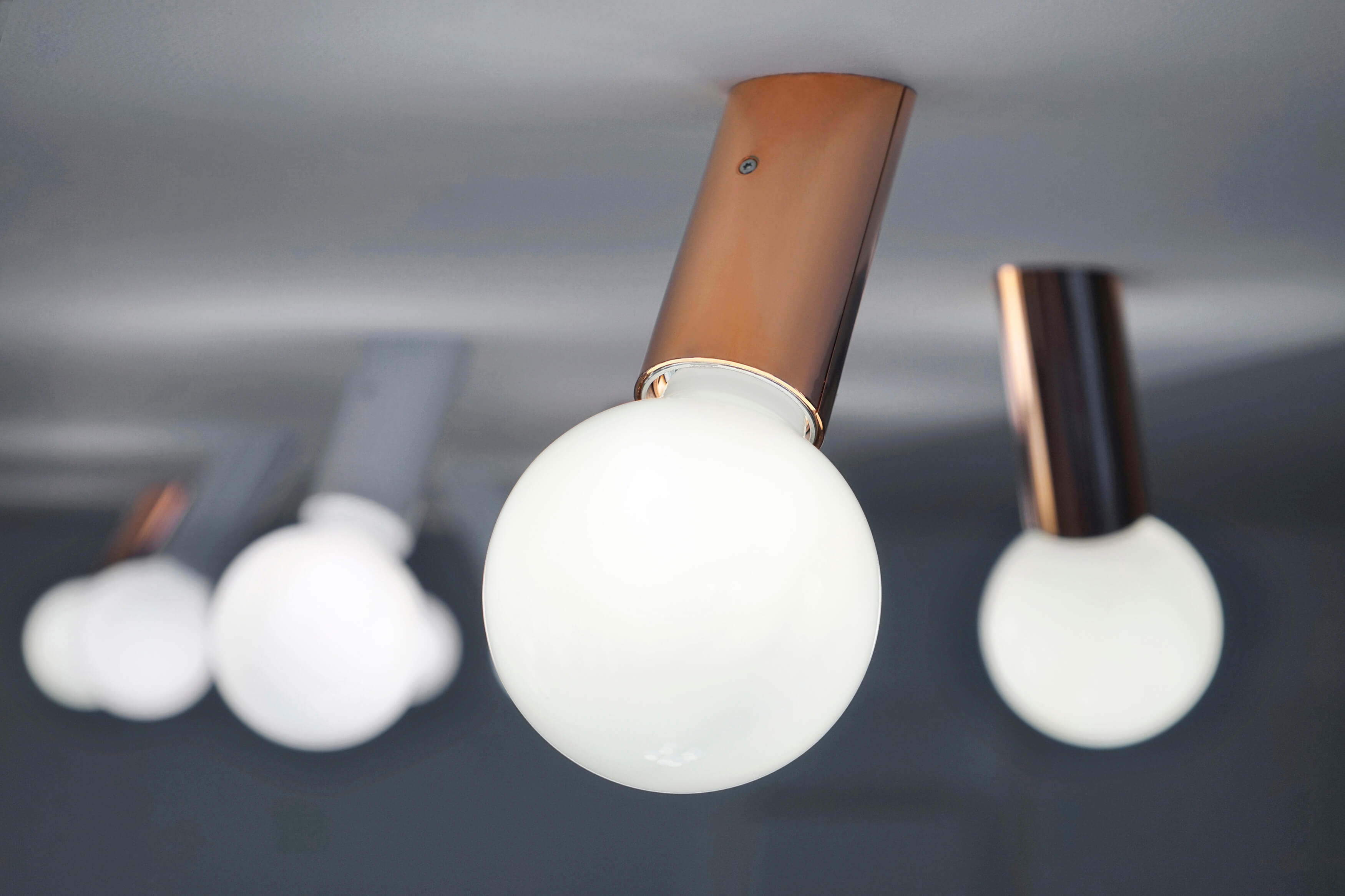 DNA Next Wandleuchte: Mehrere moderne Deckenleuchten mit runden, weißen Lampenschirmen und Kupfer-Details.