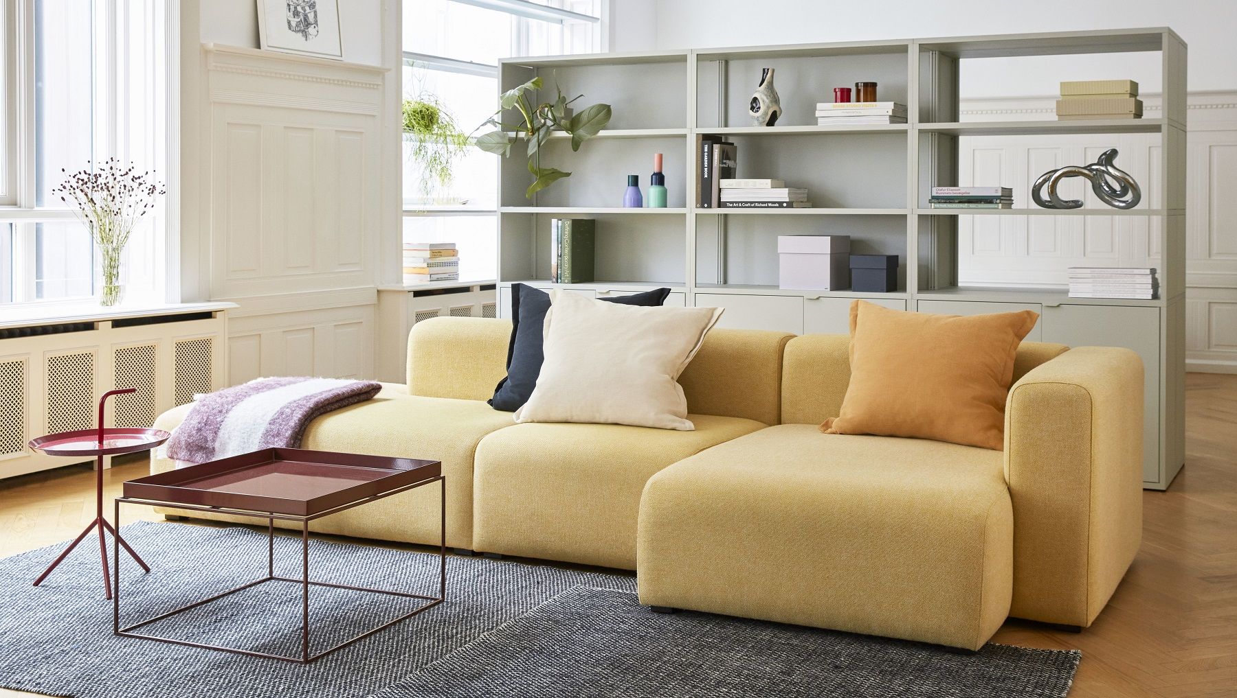Wohnzimmer-Szene mit gelbem Sofa, Bücherregal und Hay Tray Table Couchtisch mit braunem Tablett.