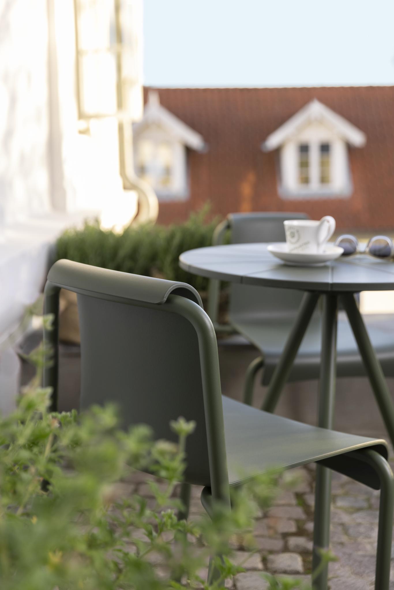 Nahaufnahme eines grünen Houe Nami Dining Chair Outdoor Stuhls mit Tisch auf einer Terrasse.