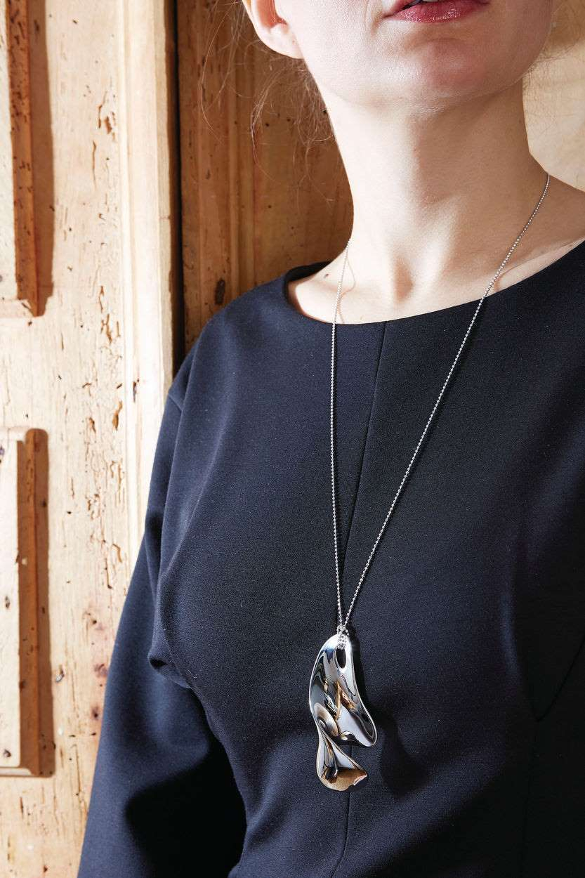 Frau mit Alessi Bulla Flaschenöffner-Kette VS01, silberfarbene Halskette mit abstraktem Anhänger, modisches Accessoire.