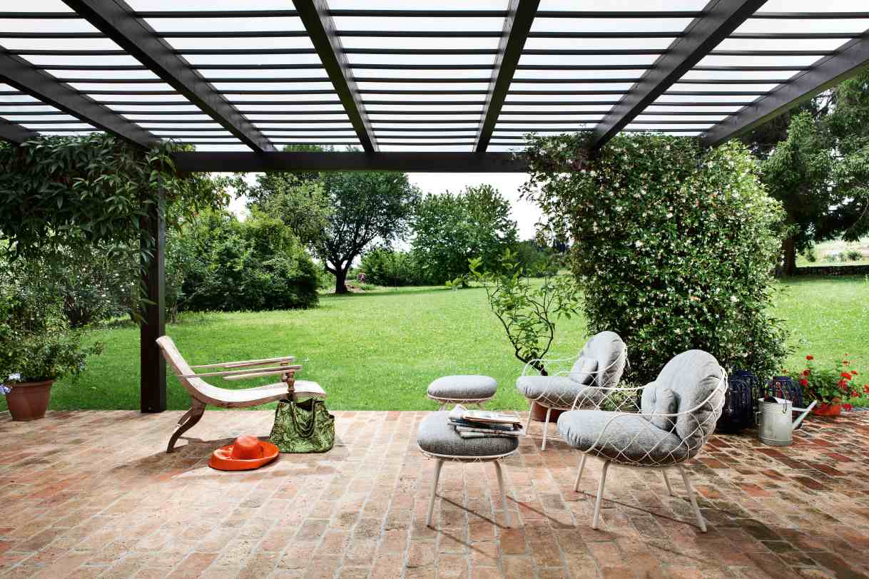 Piña Low Chair: Magis Outdoor Sessel auf einer Terrasse mit Garten im Hintergrund.