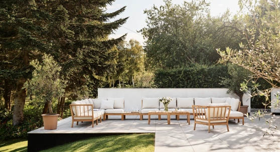 Große Gartenlounge aus Holz mit weißen Kissen und passendem Tisch auf sonniger Terrasse.