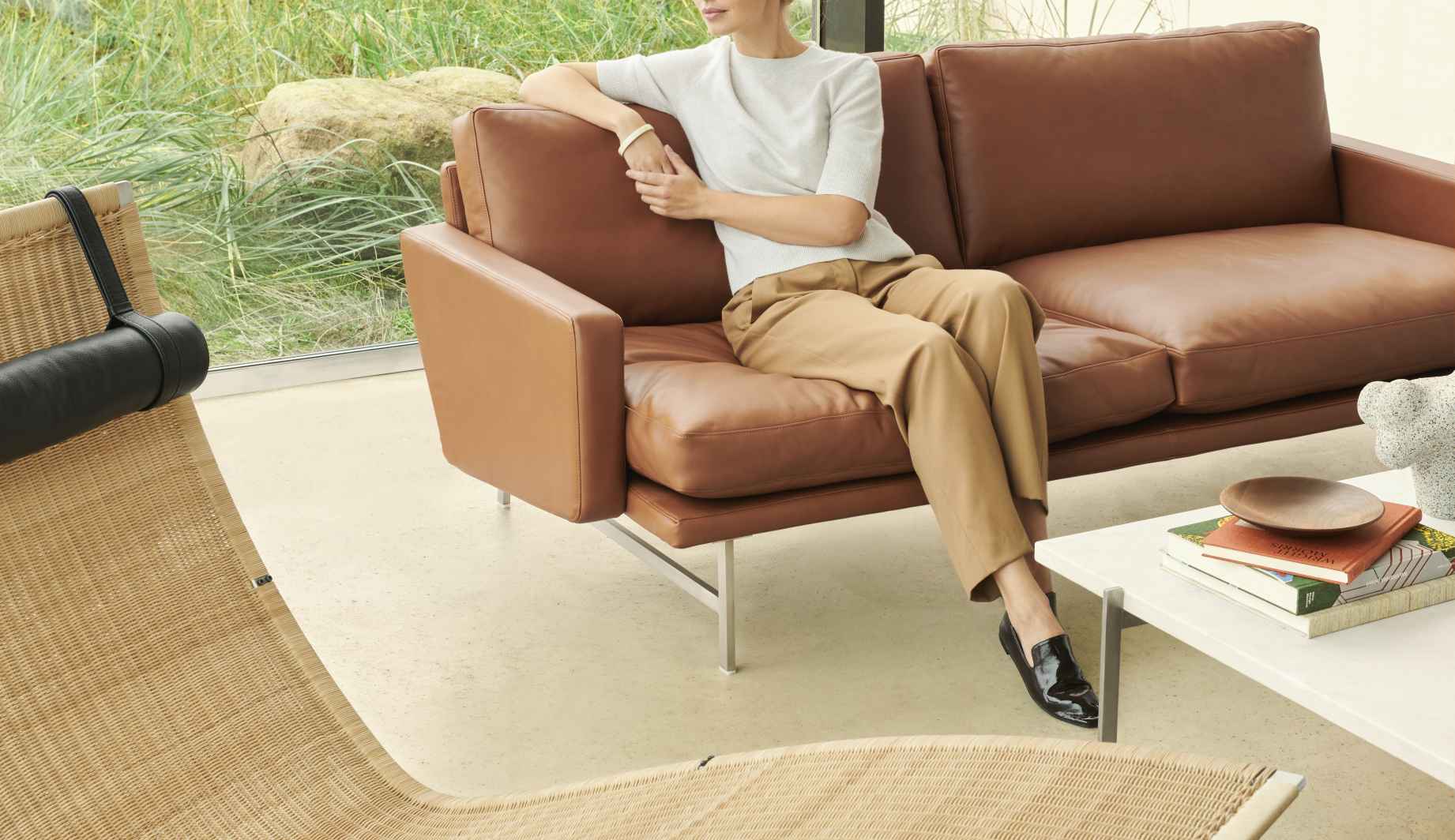 Frau entspannt auf braunem Ledersofa von Fritz Hansen, daneben die PK24 Liege. Hochwertige Designermöbel.