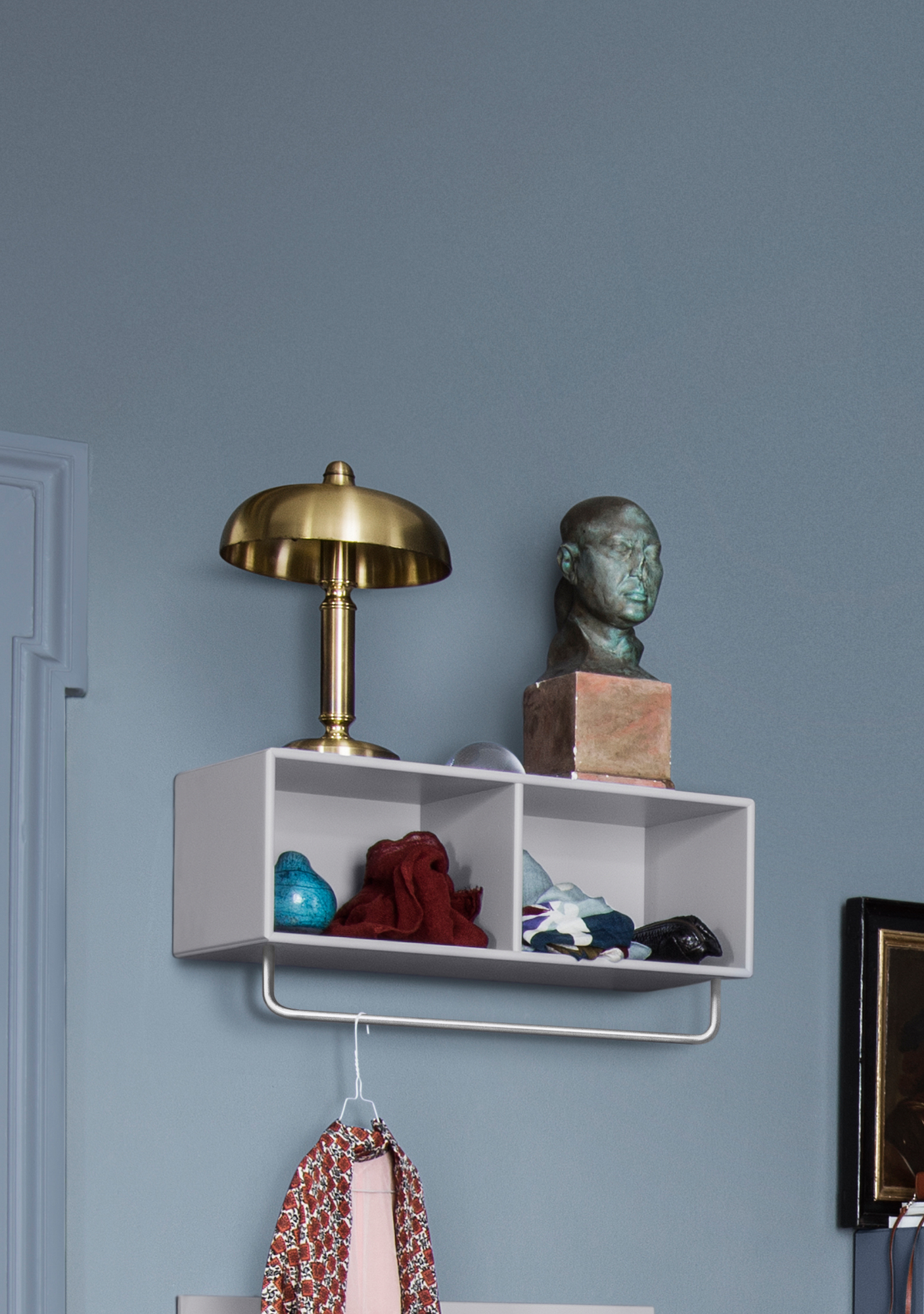 Montana Mushroom Ablage mit Kleiderstange an blauer Wand, dekoriert mit Lampe und Skulptur.