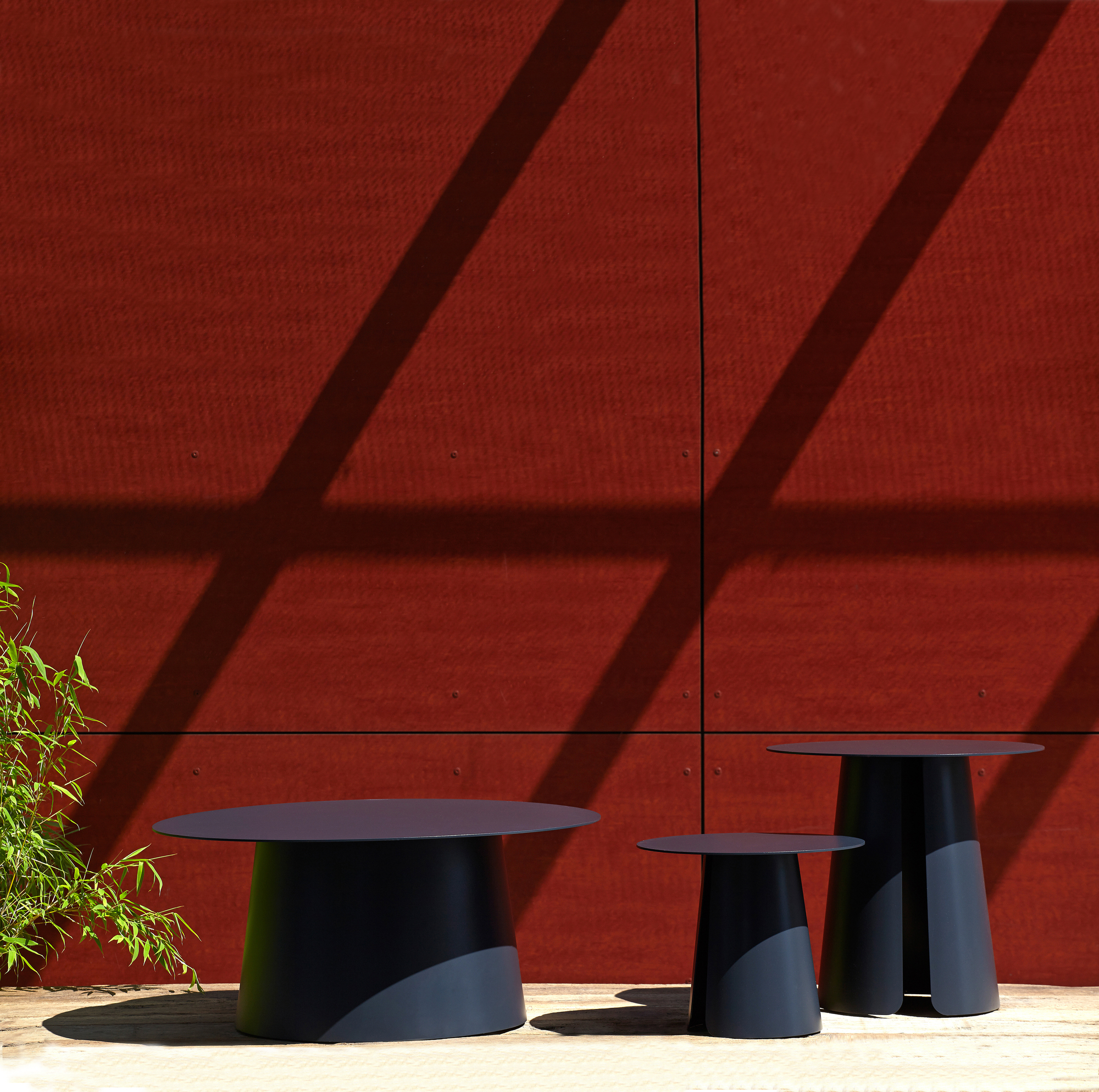 Drei schwarze Beistelltische der Serie Feel von Jan Kurtz in unterschiedlichen Größen vor roter Wand.