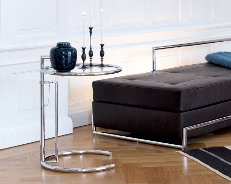 Chrom Beistelltisch mit Glasplatte, Vase und Kerzenständern neben brauner Lederbank im modernen Wohnzimmer.