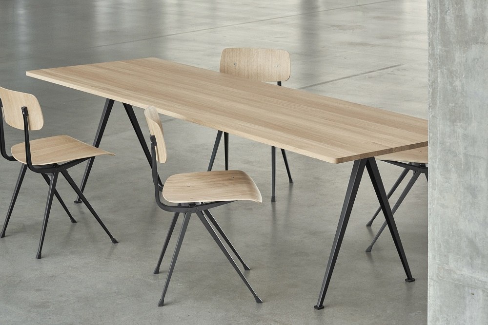 Pyramid Table 02 Esstisch von Hay mit Holzplatte und schwarzen Stahlbeinen, umgeben von Stühlen.