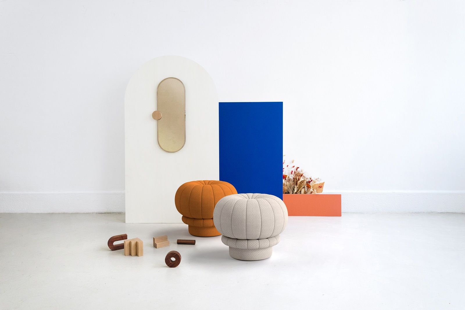 Zwei Claudie Pouf Hocker von Hartô in Orange und Beige vor farbigem Hintergrund.