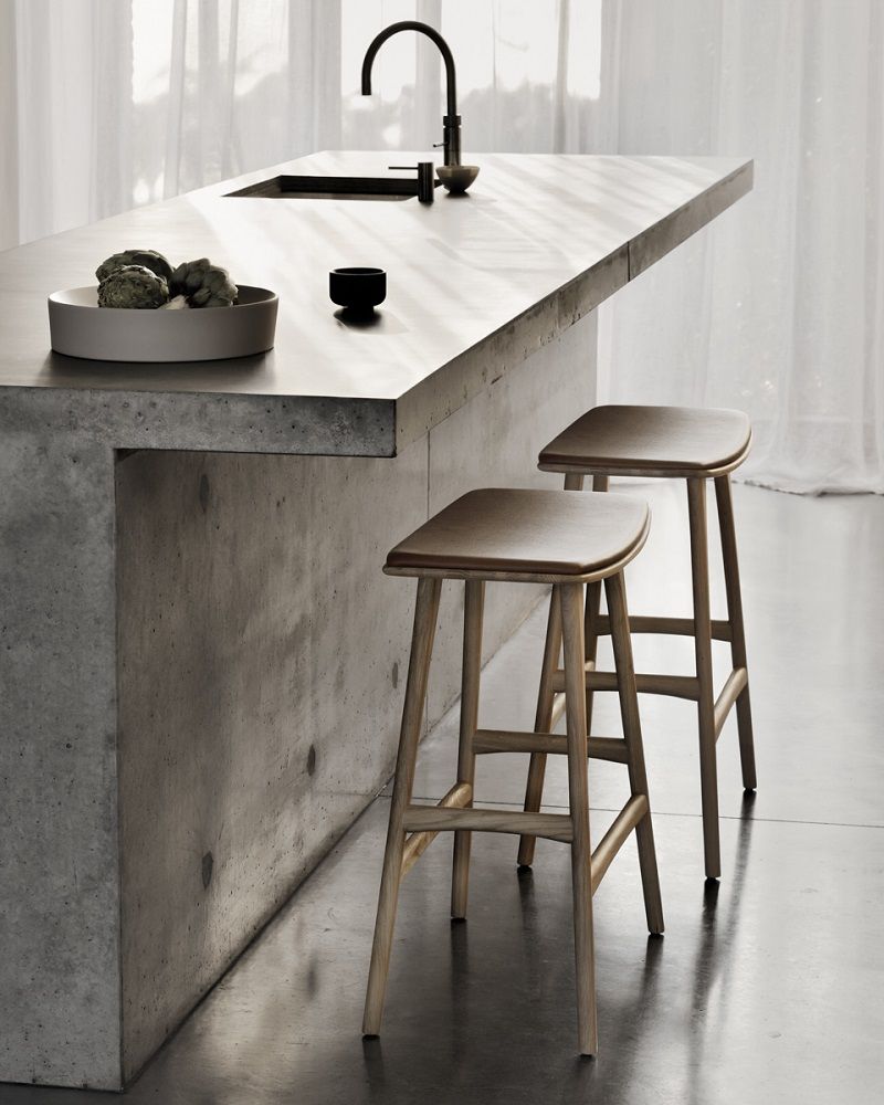 Zwei Ethnicraft Barhocker Osso mit Sitzpolster aus Holz vor einer Betoninsel.