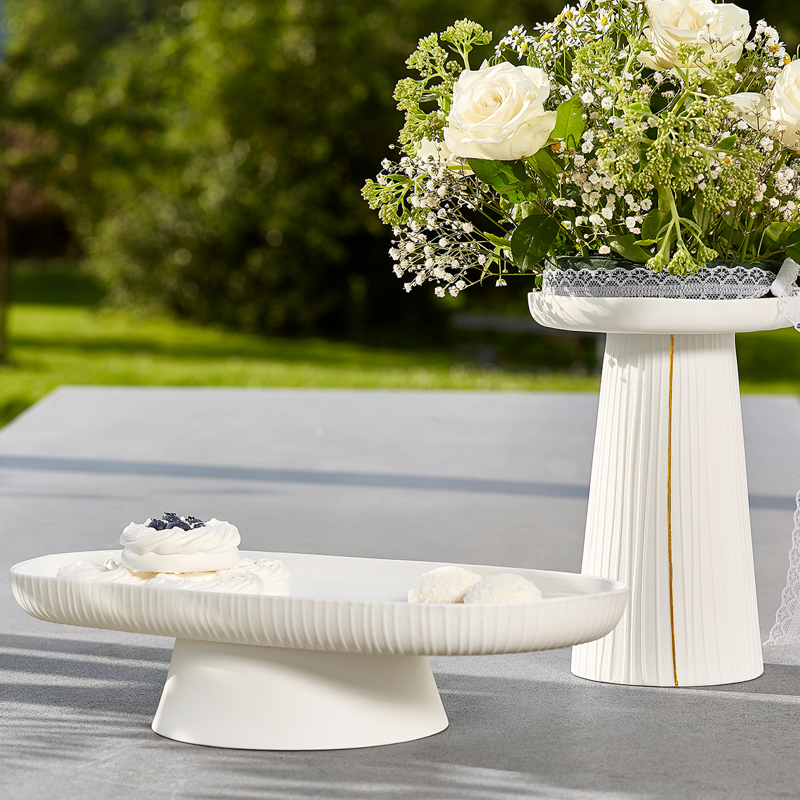 Weiße Hochzeit Anrichteplatte mit plissiertem Rand und Dessert, daneben Blumengesteck auf passender Säule.