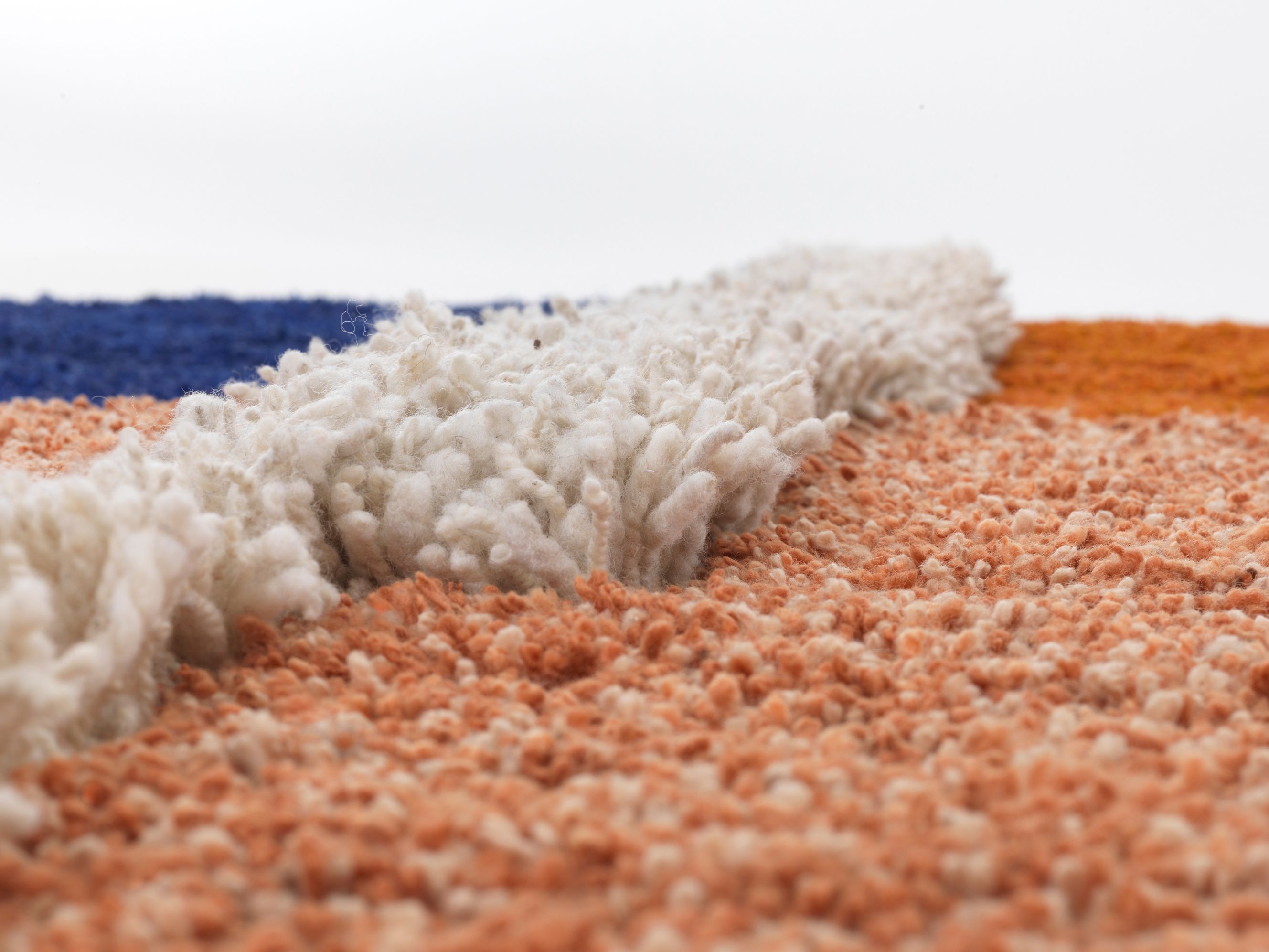 Detailaufnahme des Nudo Teppichs von Ames mit blauen, weißen und orangefarbenen Wollfasern.