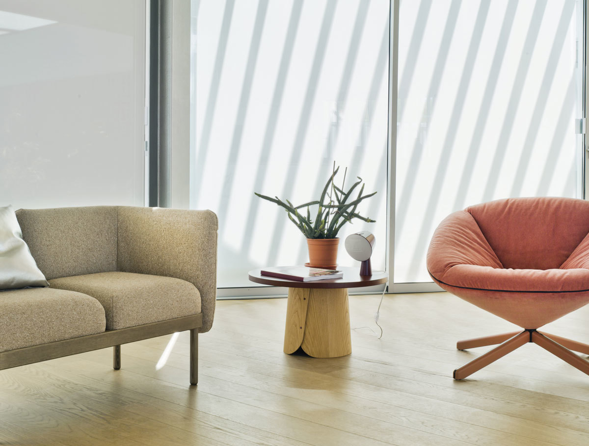 Wohnzimmer-Szene mit Sancal Tab Beistelltisch aus Holz, Lampe und Pflanze neben Sofa und Sessel.