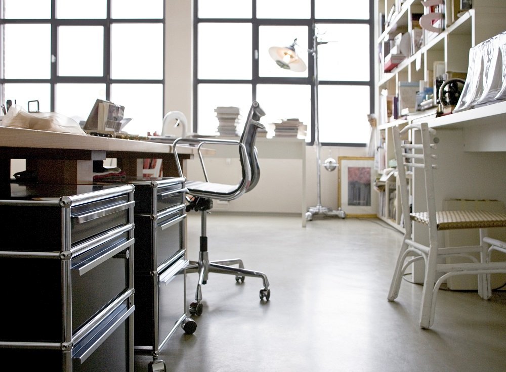 USM Haller Rollcontainer in Olivgrün mit drei Schubladen unter einem Schreibtisch in einem hellen Büro.