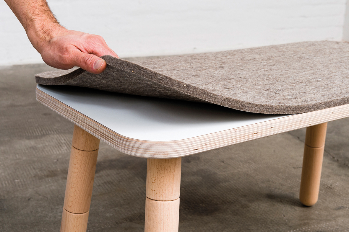 Growing Table: Hand legt grauen Sitzfilz auf eine helle Holzbank. Sitzauflage für Kinder.