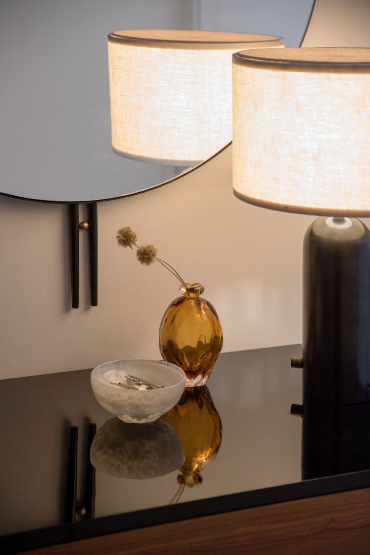 Nahaufnahme: IOI Wandspiegel Ø80 von Gubi spiegelt Lampe und Deko auf einer Kommode.