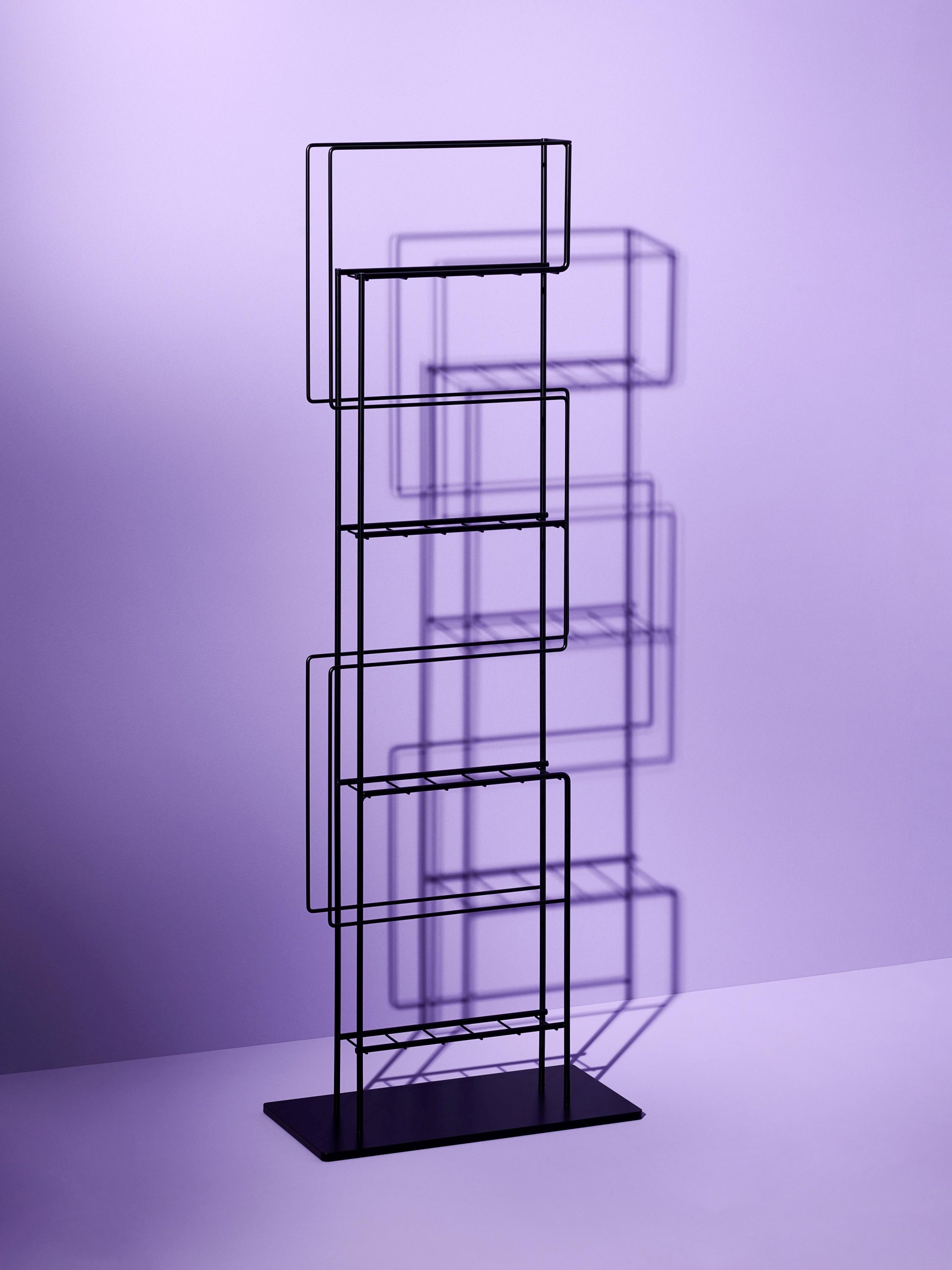 Schwarzer Schönbuch Zeitungsständer aus Metall mit mehreren Fächern vor lila Hintergrund. Design Zeitungsregal für Zeitschriften.