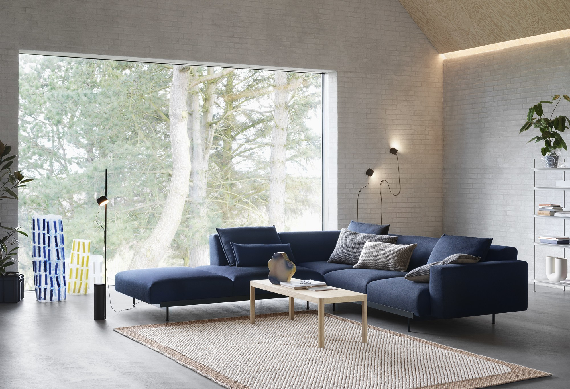 Wohnzimmer mit Muuto Post Wandleuchten und Stehleuchte, moderner Beleuchtung und blauem Sofa.